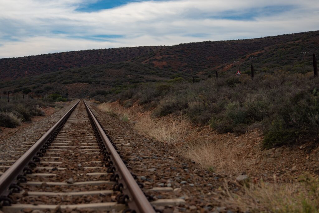 Lonely railway track through remote countryside with hills and shrubs under a cloudy sky.